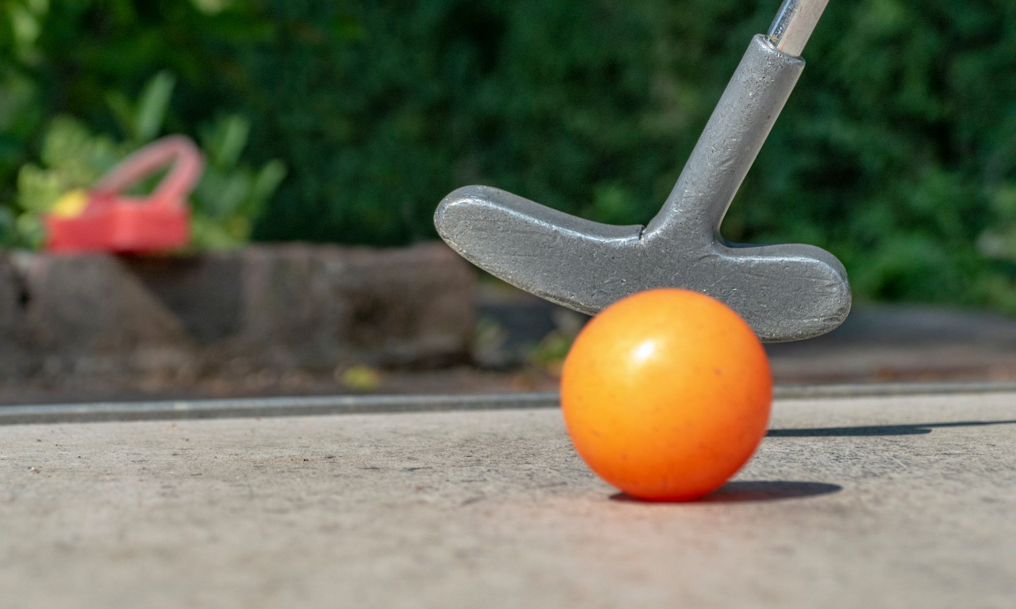 Mini golf ball and putter on a course at the beach. Ball is orange. Putter is silver color