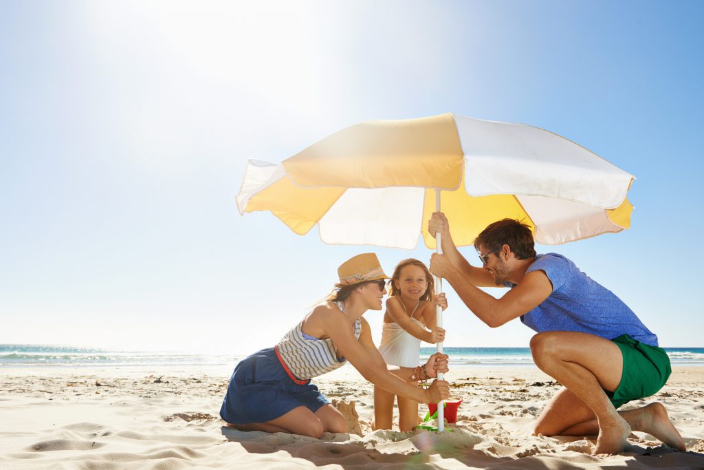 Shot of a young family setting up an umbrella on a beach