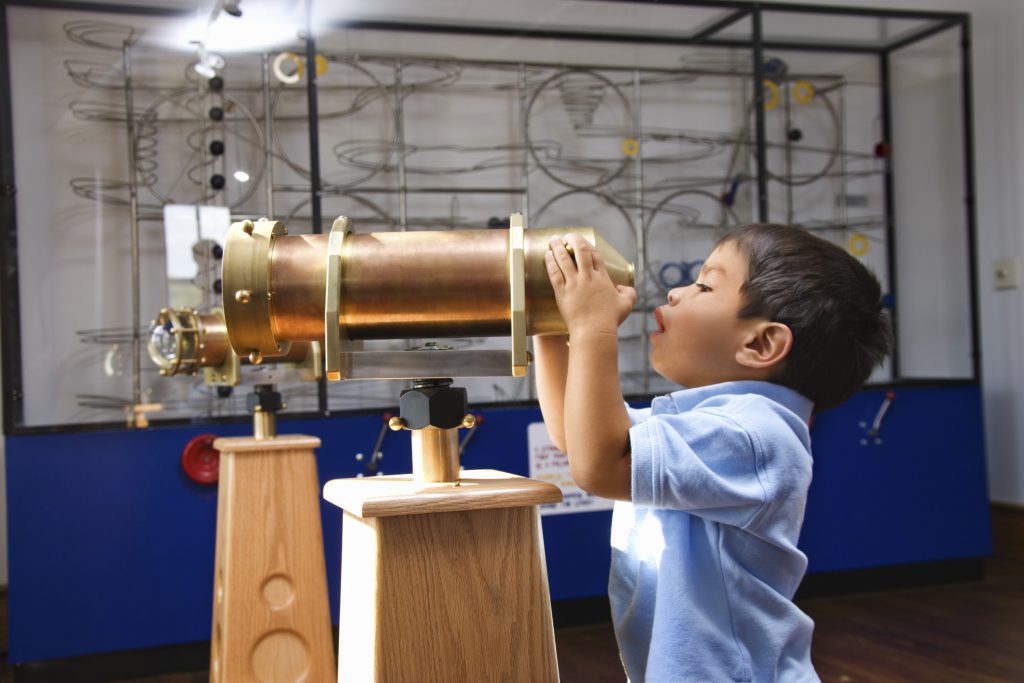 young boy looking through a telescope at a discovery museum