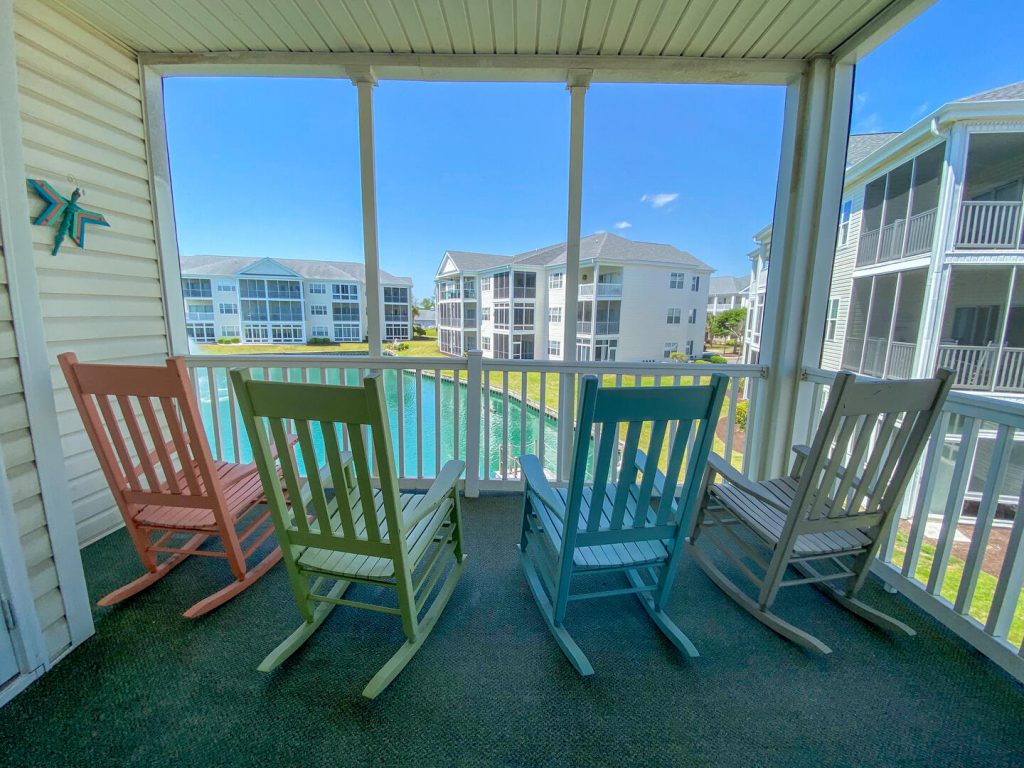 4 colorful rocking chairs on back screened in patio overlooking a small lake and other condos