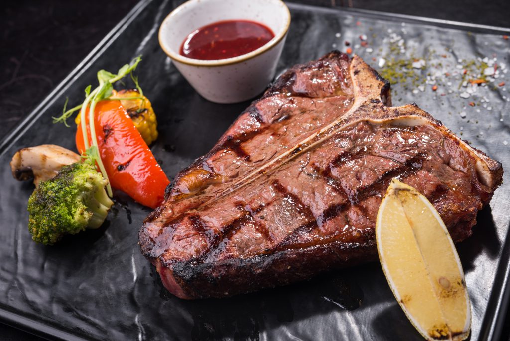 Grilled T-bone steak with vegetables on a black board. barbecue food in restaurant