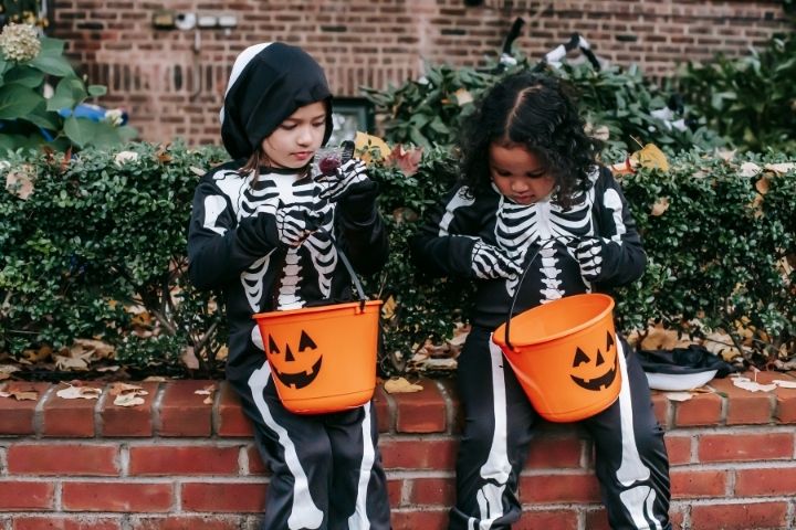 Two young children dressed as skeletons checking out their halloween candy they got from trick-or-treating